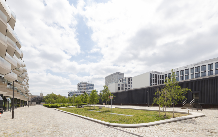 Am Hamburger Bahnhof, Berlin-Mitte. Rechts die Rieckhallen. In der Mitte ein Grünstreifen mit einigen Bäumen und links angeschnitten Balkone eines Modernen Gebäudes. Der Himmel ist bedeckt, die Lichstimmung hell.