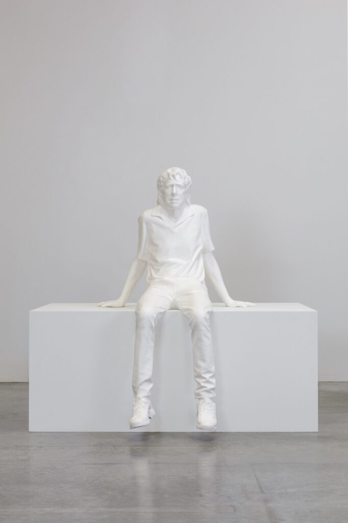 Skulptur ein weiß eines jungen Mannes, der auf einem weißen Block sitzt. Die Beine hängen herab, berühren aber nicht den Boden. Er ist leicht nach hinten gelehnt und stützt sich auf seine Hände.