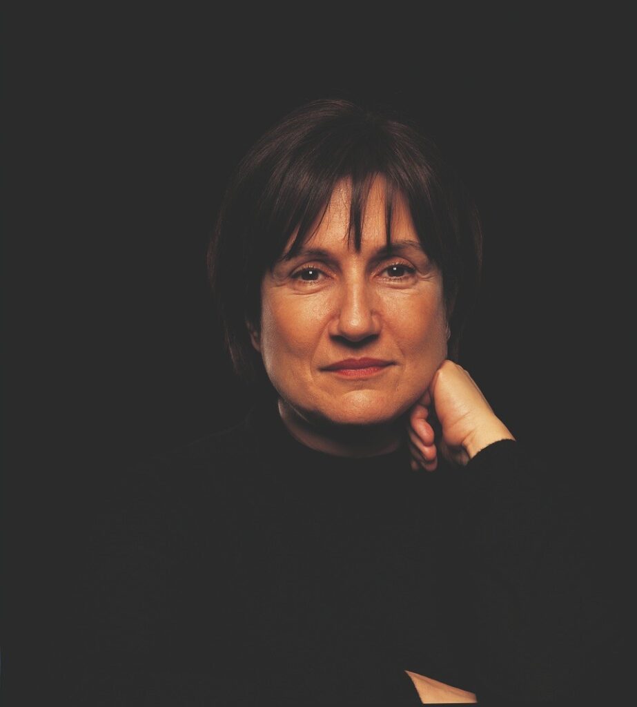 Portrait von Ayşe Erkmen. Die Künstlerin hat den Kopf leicht auf die linke Faust gestützt und blickt entspannt in die Kamera